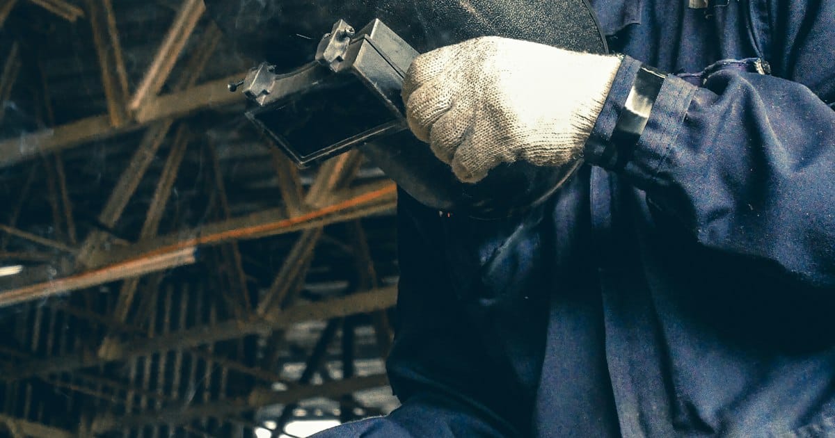 Web para fabricantes y metalúrgicas en Argentina: operario con máscara de soldar en una planta industrial